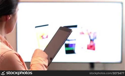 Woman watches television while holding and using tablet device.