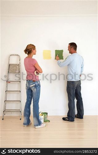 Woman watching man testing paint colours on wall