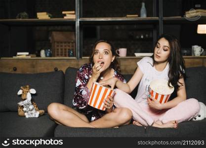 woman watching movie while her friend taking popcorn from her bucket
