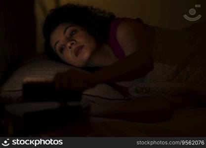 Woman watching smartphone alone at night while lying on bed 