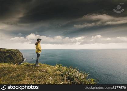 Woman watching the ocean with a lighthouse on the back, Azores Island.