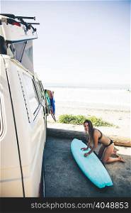 Woman waxing surfboard beside camper van
