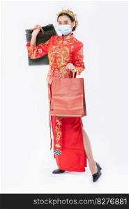 woman wear Cheongsam suit and mask hold paper bag from shopping in chinese new year 