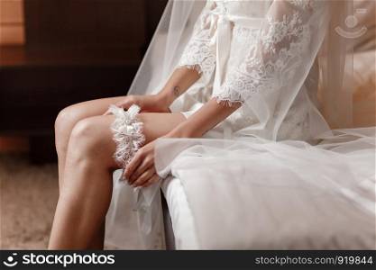 Woman wearing a garter on the leg. The bride holds in hand lose-up garter in hotel room. morning preparation wedding concept.. The bride holds in hand lose-up garter in hotel room. morning preparation wedding concept.