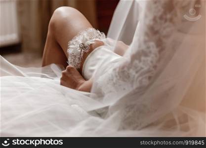 Woman wearing a garter on the leg. The bride holds in hand lose-up garter in hotel room. morning preparation wedding concept.. The bride holds in hand lose-up garter in hotel room. morning preparation wedding concept.