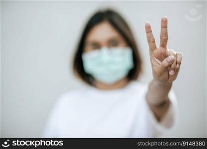 Woman wearing a mask and lift two fingers. Selective focus.