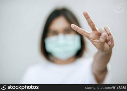 Woman wearing a mask and lift two fingers. Selective focus.