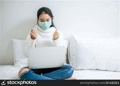 Woman wearing a mask, sitting on the bed and playing laptop.