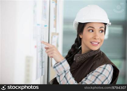 woman wearing a safety helmet pointing to notice board
