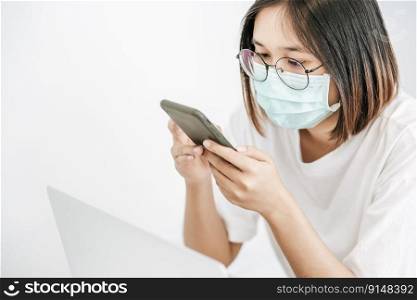 Woman wearing a sanitary mask, playing a smartphone and having a laptop.