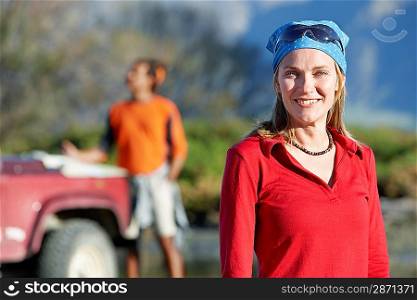Woman wearing bandana with man by car behind outdoors focus on woman