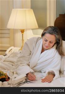Woman wearing bathrobe writing lying on bed