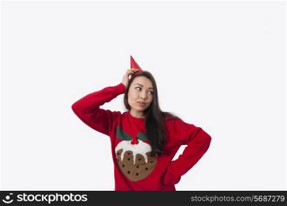 Woman wearing Christmas jumper and party hat against gray background
