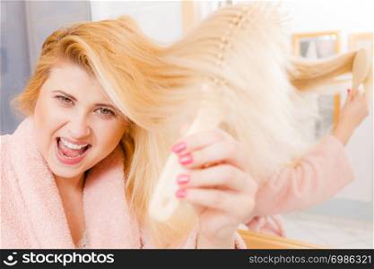 Woman wearing dressing gown brushing her long blonde hair, morning beauty routine. Haircare and hairstyling concept.. Woman wearing dressing gown brushing her hair