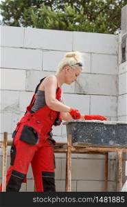 Woman wearing dungarees working on construction site of her home. Mixing cement in bowl preparing mortar.. Woman working on home construction site