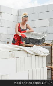 Woman wearing dungarees working on construction site of her home. Mixing cement in bowl preparing mortar.. Woman working on home construction site