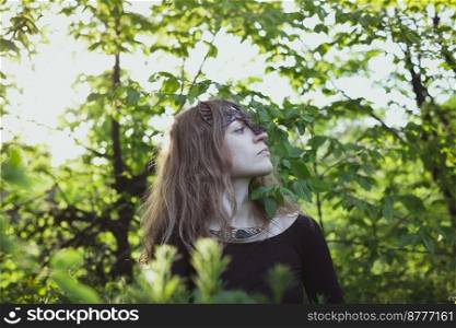 Woman wearing fantastic druid bird mask scenic photography. Picture of beautiful lady with green landscape on background. High quality wallpaper. Photo concept for ads, travel blog, magazine, article. Woman wearing fantastic druid bird mask scenic photography