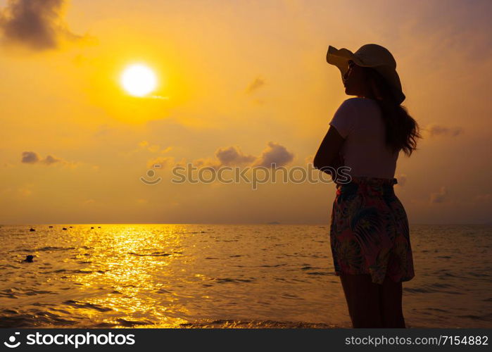 woman wearing hat standing on the sea beach at sunset