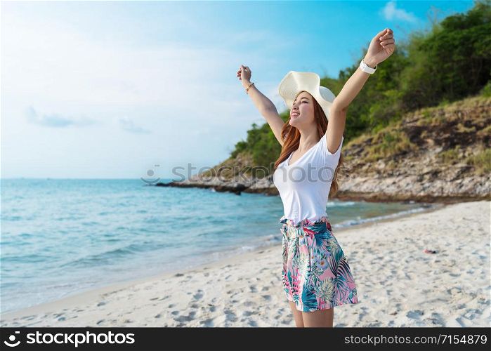 woman wearing hat with arms raised standing on the sea beach