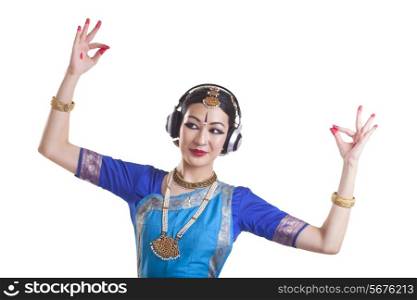 Woman wearing headphone while performing Bharatanatyam over white background