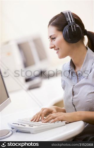 Woman wearing headphones in computer room typing and smiling