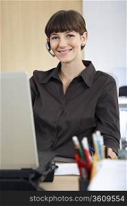 Woman wearing headset at desk in office, portrait