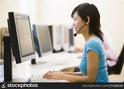 Woman wearing headset in computer room typing and smiling