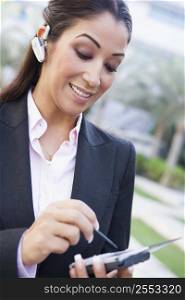 Woman wearing headset outdoors and using personal digital assistant smiling (selective focus)