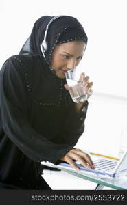 Woman wearing headset with laptop drinking water and smiling (high key/selective focus)