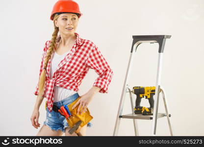Woman wearing helmet using drill. Girl working at flat remodeling. Building, repair and renovation.. Woman wearing helmet using drill