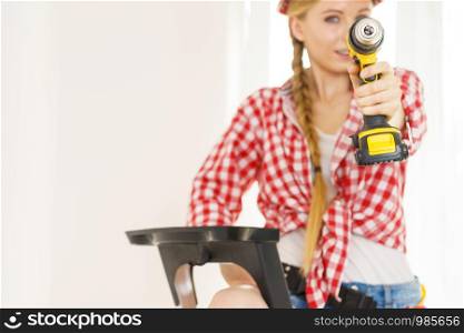 Woman wearing helmet using drill. Girl working at flat remodeling. Building, repair and renovation.. Woman wearing helmet using drill