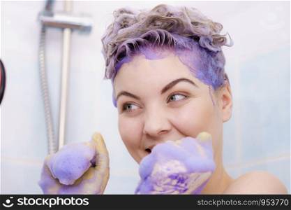 Woman wearing latex protective gloves while applying purple toner shampoo on her blonde hair. Haircare coloring at home concept.. Woman applying toner shampoo on her hair