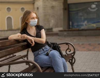 woman wearing medical mask outside while sitting bench