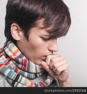 woman wearing multicolored scarf around neck coughing against gray backdrop