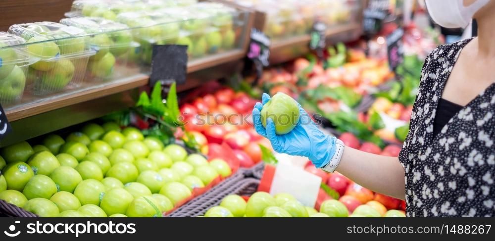 woman wearing nitrile gloves and holding green apple fruit in supermarket or grocery, protect coronavirus inflection. Hygiene, new normal and life after covid-19 pandemic