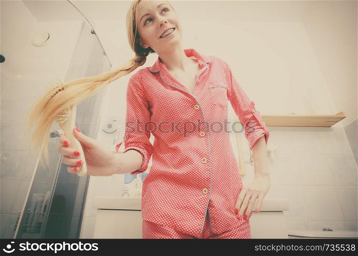 Woman wearing pajamas in bathroom having fun while brushing her long blonde hair, braided hairdo, shot from bottom.. Woman brushing her long hair