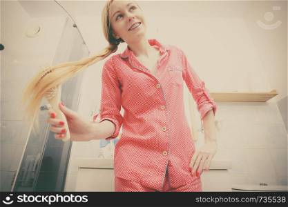 Woman wearing pajamas in bathroom having fun while brushing her long blonde hair, braided hairdo, shot from bottom.. Woman brushing her long hair