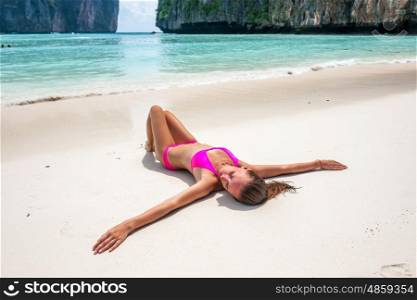Woman wearing pink bikini laying on tropical beach at Thailand with arms outstretched