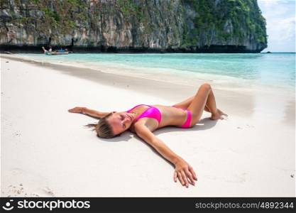 Woman wearing pink bikini laying on tropical beach at Thailand with arms outstretched