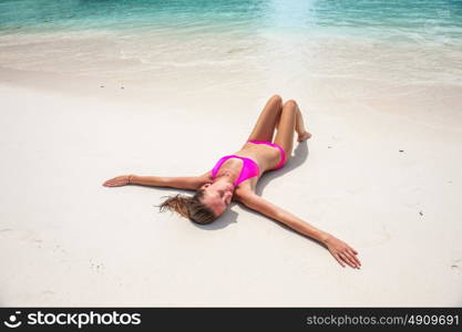 Woman wearing pink bikini laying on tropical beach at Thailand with arms outstretched