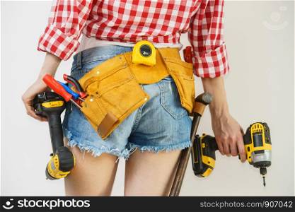 Woman wearing protective workwear toolbelt using drill. Girl working at flat remodeling. Building, repair and renovation.. Woman with toolbelt and drill