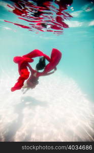 Woman wearing red dress,draped in red fabric, floating underwater
