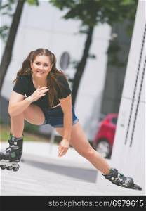 Woman wearing roller skates riding in town. Female being sporty stretching her legs before long ride.. Young woman riding roller skates