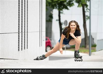 Woman wearing roller skates riding in town. Female being sporty stretching her legs before long ride.. Young woman riding roller skates