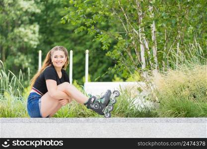 Woman wearing roller skates sitting in park. Female relaxing after a long ride.. Young woman riding roller skates