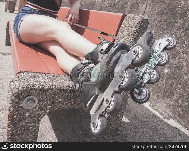 Woman wearing roller skates sitting on bench with raised legs. Bizarre angle. Woman on bench wearing roller skates