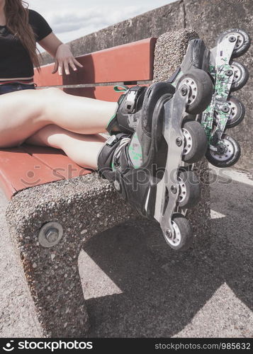 Woman wearing roller skates sitting on bench with raised legs. Bizarre angle. Woman on bench wearing roller skates