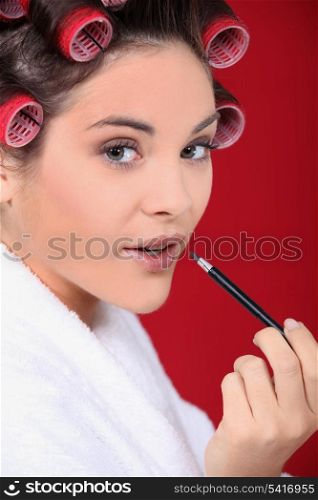Woman wearing rollers and applying lip gloss