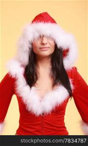 woman wearing santa claus costume clothes covering her eyes with christmas hat, pulling down the hat over the eyes on yellow background
