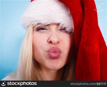 Woman wearing Santa Claus hat making funny face expressions. Christmas fun and celebration concept. Studio shot on blue background.. Woman wearing Santa Claus hat making faces